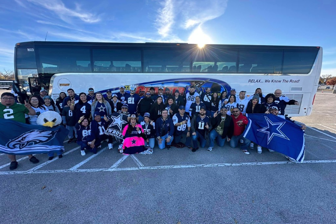 A group of people standing in front of a Dallas Cowboys tour bus