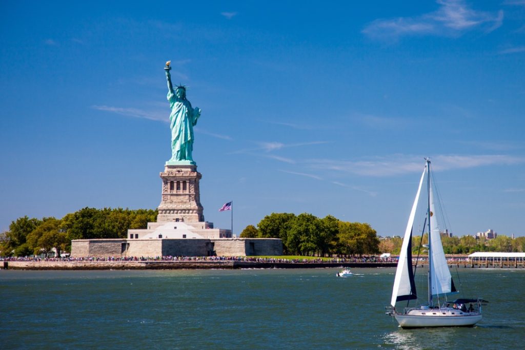 Liberty Island, New York City, USA - 08.24.2013: A sailboat sails slowly by Liberty Island where the famous Statue of Liberty, France's gift to the United States, stands