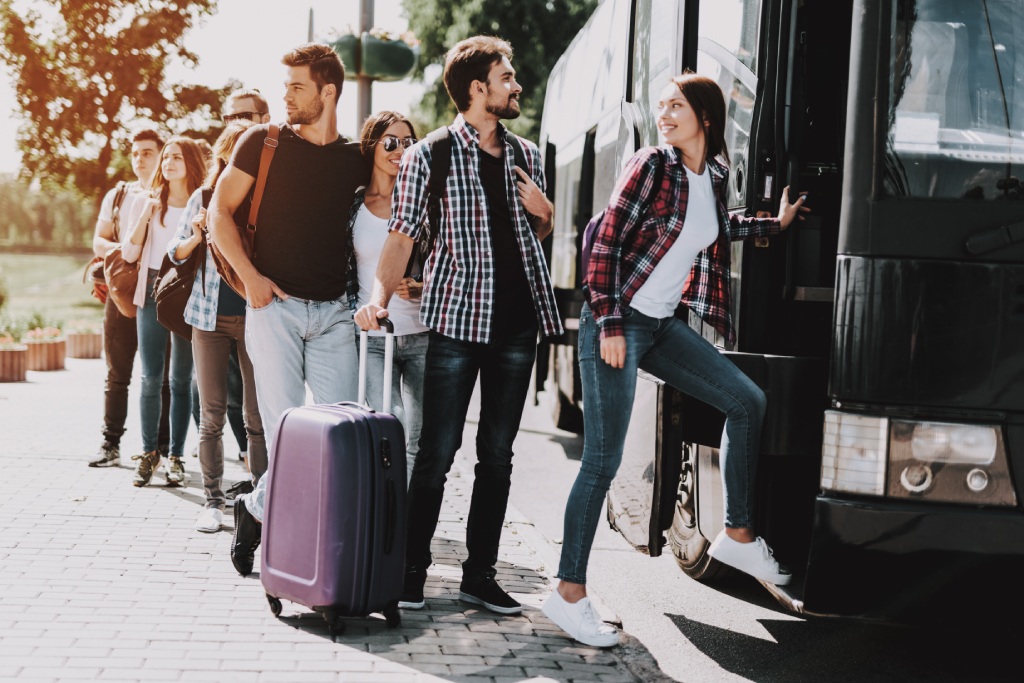 Group of Young People Boarding on Travel Bus. Happy Travelers Standing in Queue Holding Luggage Waiting their turn to Enter Bus. Traveling, Tourism and People Concept. Summer Vacation